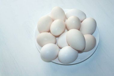 Beyaz arka planda beyaz bir tabakta istiflenmiş kocaman beyaz tavuk yumurtaları..