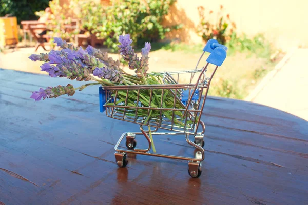 Lavender flowers in a mini supermarket cart on a wooden surface.