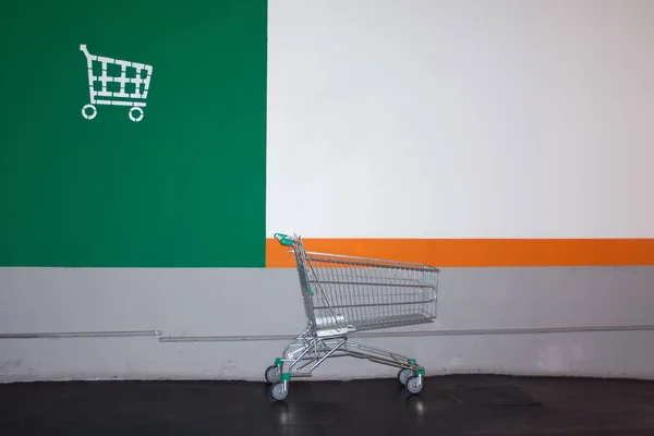 A lone supermarket cart stands next to the wall marked with the cart logo.