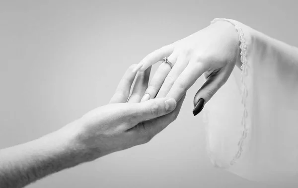 Hands of man and woman reaching to each other on gray background. Black and white photo