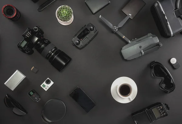 Work space photographer with laptop, digital camera, memory card, action camera, drone, remote controller, phone, VR glasses and camera accessory. Top view on black table background. Concept of mockup template.