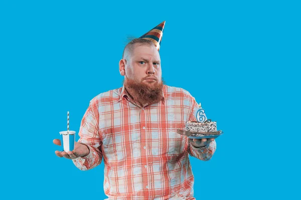 Adult man with birthday cap holding a cake on blue background. Studio photo shooting