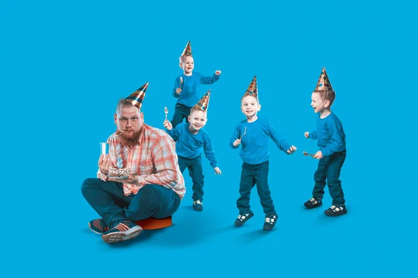 En un malentendido, un hombre adulto con niños felices en una gorra de fiesta, sosteniendo un pastel en el cumpleaños de un niño sobre un fondo azul. Concepto de vacaciones foto estudio rodaje . — Foto de Stock