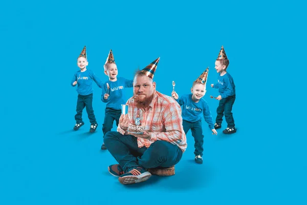 En un malentendido, un hombre adulto con niños felices en una gorra de fiesta, sosteniendo un pastel en el cumpleaños de un niño sobre un fondo azul. Concepto de vacaciones foto estudio rodaje . — Foto de Stock
