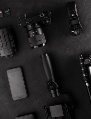 Bilgisayarı, dijital kamerası, hafıza kartı, aksiyon kamerası, drone 'u, uzaktan kumandası, telefonu ve kamera aksesuarı olan bir çalışma alanı kameramanı. Siyah tablo arkaplanındaki üst görünüm.