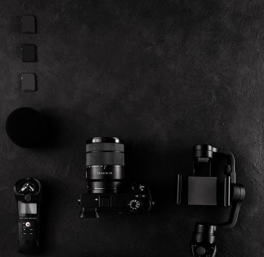 Bilgisayarı, dijital kamerası, hafıza kartı, aksiyon kamerası, drone 'u, uzaktan kumandası, telefonu ve kamera aksesuarı olan bir çalışma alanı kameramanı. Siyah tablo arkaplanındaki üst görünüm.