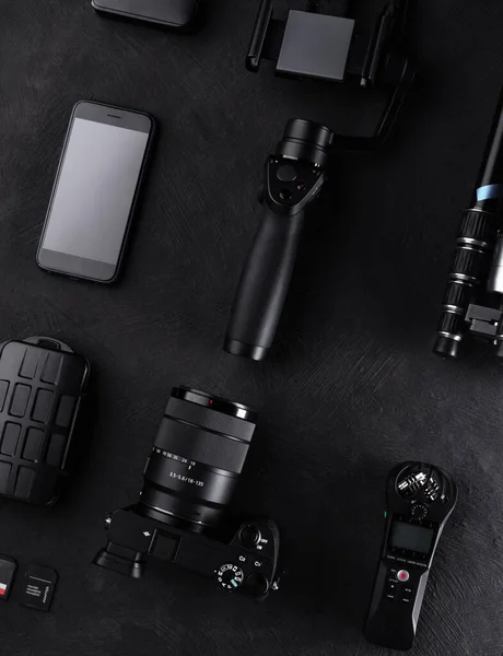 Work space videographer with laptop, digital camera, memory card, action camera, drone, remote controller, phone and camera accessory. Top view on black table background.