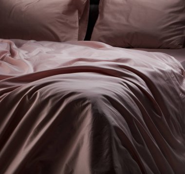 A beautifully arranged soft pink bedding is draped over a modern bed in a stylish bedroom. The fabric creates a warm and inviting ambiance that enhances the decor.