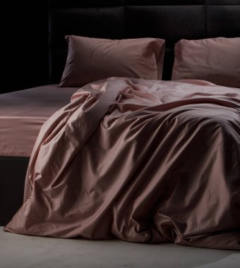Soft pink bedding is elegantly draped over a sleek black bed frame in a cozy bedroom, illuminated by gentle evening light, creating a serene atmosphere.