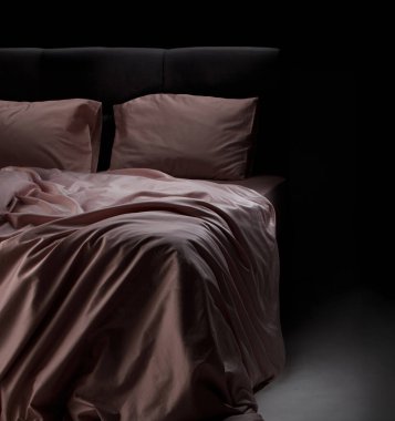 Soft pink bedding is elegantly draped over a sleek black bed frame in a cozy bedroom, illuminated by gentle evening light, creating a serene atmosphere.