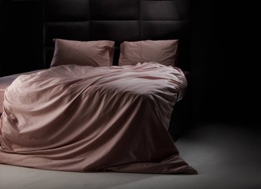 Soft pink bedding is elegantly draped over a sleek black bed frame in a cozy bedroom, illuminated by gentle evening light, creating a serene atmosphere.