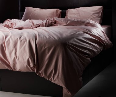 Soft pink bedding is elegantly draped over a sleek black bed frame in a cozy bedroom, illuminated by gentle evening light, creating a serene atmosphere.