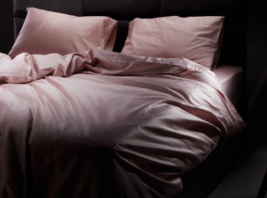 Soft pink bedding is elegantly draped over a sleek black bed frame in a cozy bedroom, illuminated by gentle evening light, creating a serene atmosphere.