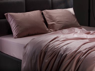 Luxurious pale pink bedding adorns a contemporary bed, featuring smooth pillows and sheets that create a cozy and inviting atmosphere in a stylish bedroom.