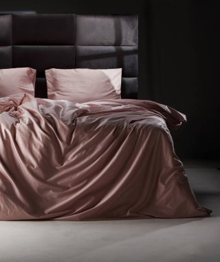 The cozy bed features soft pink linens and pillows, perfectly unmade. The modern headboard and neutral background enhance the inviting atmosphere of the room.