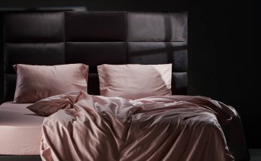 The cozy bed features soft pink linens and pillows, perfectly unmade. The modern headboard and neutral background enhance the inviting atmosphere of the room.