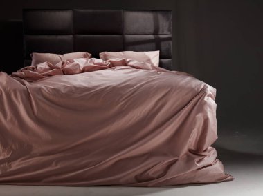 The cozy bed features soft pink linens and pillows, perfectly unmade. The modern headboard and neutral background enhance the inviting atmosphere of the room.