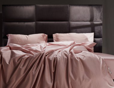 The cozy bed features soft pink linens and pillows, perfectly unmade. The modern headboard and neutral background enhance the inviting atmosphere of the room.