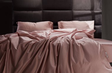 The cozy bed features soft pink linens and pillows, perfectly unmade. The modern headboard and neutral background enhance the inviting atmosphere of the room.