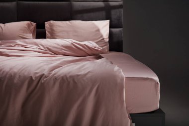 The cozy bed features soft pink linens and pillows, perfectly unmade. The modern headboard and neutral background enhance the inviting atmosphere of the room.