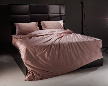 The cozy bed features soft pink linens and pillows, perfectly unmade. The modern headboard and neutral background enhance the inviting atmosphere of the room.