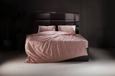 The cozy bed features soft pink linens and pillows, perfectly unmade. The modern headboard and neutral background enhance the inviting atmosphere of the room.