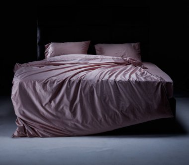 The cozy bed features soft pink linens and pillows, perfectly unmade. The modern headboard and neutral background enhance the inviting atmosphere of the room.