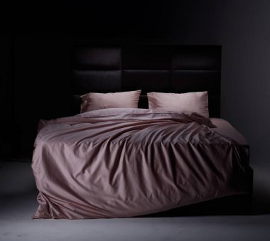 The cozy bed features soft pink linens and pillows, perfectly unmade. The modern headboard and neutral background enhance the inviting atmosphere of the room.