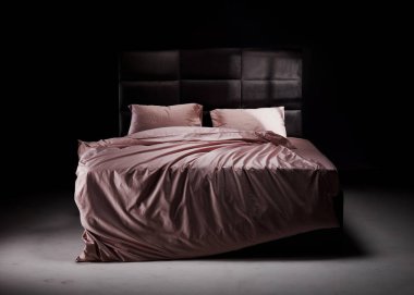 The cozy bed features soft pink linens and pillows, perfectly unmade. The modern headboard and neutral background enhance the inviting atmosphere of the room.