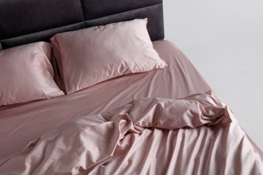 A perfectly arranged bed features soft pink sheets and matching pillows in a clean and minimalist bedroom. The inviting space conveys comfort and relaxation, ideal for restful evenings.