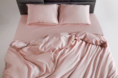 A perfectly arranged bed features soft pink sheets and matching pillows in a clean and minimalist bedroom. The inviting space conveys comfort and relaxation, ideal for restful evenings.