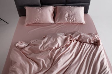 A perfectly arranged bed features soft pink sheets and matching pillows in a clean and minimalist bedroom. The inviting space conveys comfort and relaxation, ideal for restful evenings.