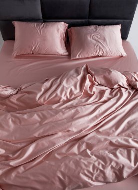 A perfectly arranged bed features soft pink sheets and matching pillows in a clean and minimalist bedroom. The inviting space conveys comfort and relaxation, ideal for restful evenings.