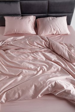 A perfectly arranged bed features soft pink sheets and matching pillows in a clean and minimalist bedroom. The inviting space conveys comfort and relaxation, ideal for restful evenings.
