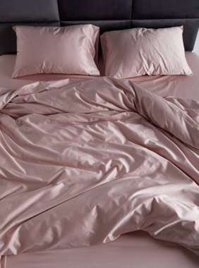 A perfectly arranged bed features soft pink sheets and matching pillows in a clean and minimalist bedroom. The inviting space conveys comfort and relaxation, ideal for restful evenings.