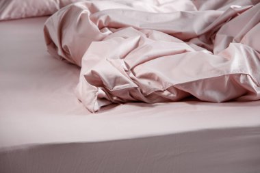 A neatly made bed showcases soft pink bedding with crumpled sheets and pillows, highlighting a modern bedroom's tranquil and inviting ambiance during daylight hours.
