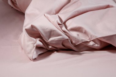 A neatly made bed showcases soft pink bedding with crumpled sheets and pillows, highlighting a modern bedroom's tranquil and inviting ambiance during daylight hours.