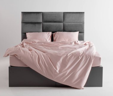 A chic bedroom showcases a sleek bed with a modern gray headboard. The soft pink bedding adds warmth, creating a cozy and inviting atmosphere in a minimalist setting.