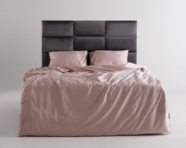 A chic bedroom showcases a sleek bed with a modern gray headboard. The soft pink bedding adds warmth, creating a cozy and inviting atmosphere in a minimalist setting.