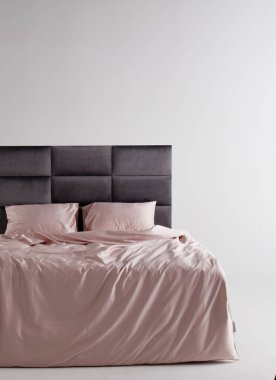 A sleek black bed frame complements soft pink sheets and pillows, creating a tranquil atmosphere in a minimally decorated bedroom space. Soft lighting enhances the peaceful environment.