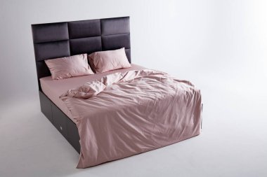 A sleek black bed frame complements soft pink sheets and pillows, creating a tranquil atmosphere in a minimally decorated bedroom space. Soft lighting enhances the peaceful environment.