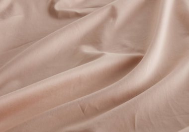 Yumuşak bej kumaş pürüzsüz bir yüzeyde, zarif örtüsünü ve ince kırışıklıklarını sergiliyor. Doğal ışık dokusunu vurgulayarak sıcak ve davetkar bir atmosfer yaratır..