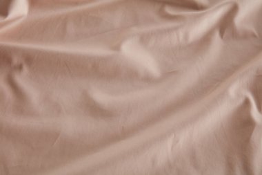 Yumuşak bej kumaş pürüzsüz bir yüzeyde, zarif örtüsünü ve ince kırışıklıklarını sergiliyor. Doğal ışık dokusunu vurgulayarak sıcak ve davetkar bir atmosfer yaratır..