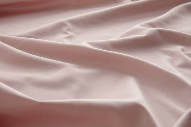 Yumuşak pembe bir kumaş düz bir yüzeyde hafifçe buruşmuş, doğal ışığı yakalıyor ve pürüzsüz dokusunu ve nazik kıvrımlarını vurguluyor, sakin bir atmosfer yaratıyor..