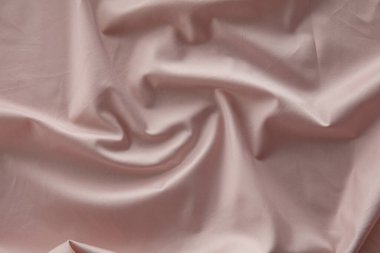 Yumuşak pembe bir kumaş düz bir yüzeyde hafifçe buruşmuş, doğal ışığı yakalıyor ve pürüzsüz dokusunu ve nazik kıvrımlarını vurguluyor, sakin bir atmosfer yaratıyor..