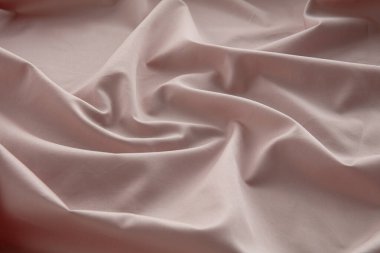Yumuşak pembe bir kumaş düz bir yüzeyde hafifçe buruşmuş, doğal ışığı yakalıyor ve pürüzsüz dokusunu ve nazik kıvrımlarını vurguluyor, sakin bir atmosfer yaratıyor..