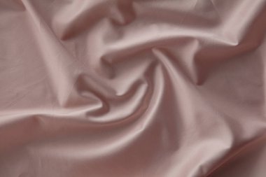 Yumuşak pembe bir kumaş düz bir yüzeyde hafifçe buruşmuş, doğal ışığı yakalıyor ve pürüzsüz dokusunu ve nazik kıvrımlarını vurguluyor, sakin bir atmosfer yaratıyor..