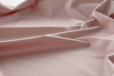 Yumuşak pembe bir kumaş düz bir yüzeyde hafifçe buruşmuş, doğal ışığı yakalıyor ve pürüzsüz dokusunu ve nazik kıvrımlarını vurguluyor, sakin bir atmosfer yaratıyor..