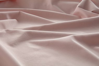 Yumuşak pembe bir kumaş düz bir yüzeyde hafifçe buruşmuş, doğal ışığı yakalıyor ve pürüzsüz dokusunu ve nazik kıvrımlarını vurguluyor, sakin bir atmosfer yaratıyor..