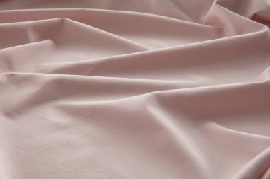 Yumuşak pembe bir kumaş düz bir yüzeyde hafifçe buruşmuş, doğal ışığı yakalıyor ve pürüzsüz dokusunu ve nazik kıvrımlarını vurguluyor, sakin bir atmosfer yaratıyor..